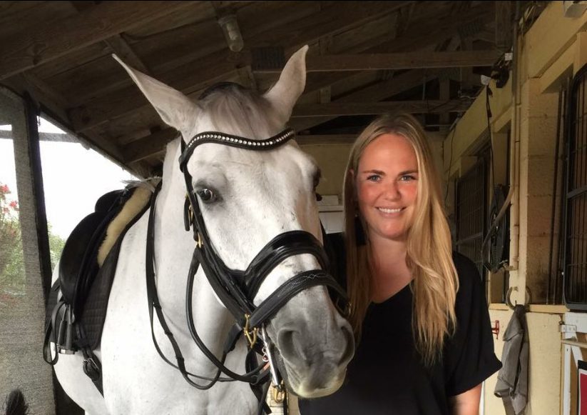 A woman with long, blonde hair, taking a picture with a white horse